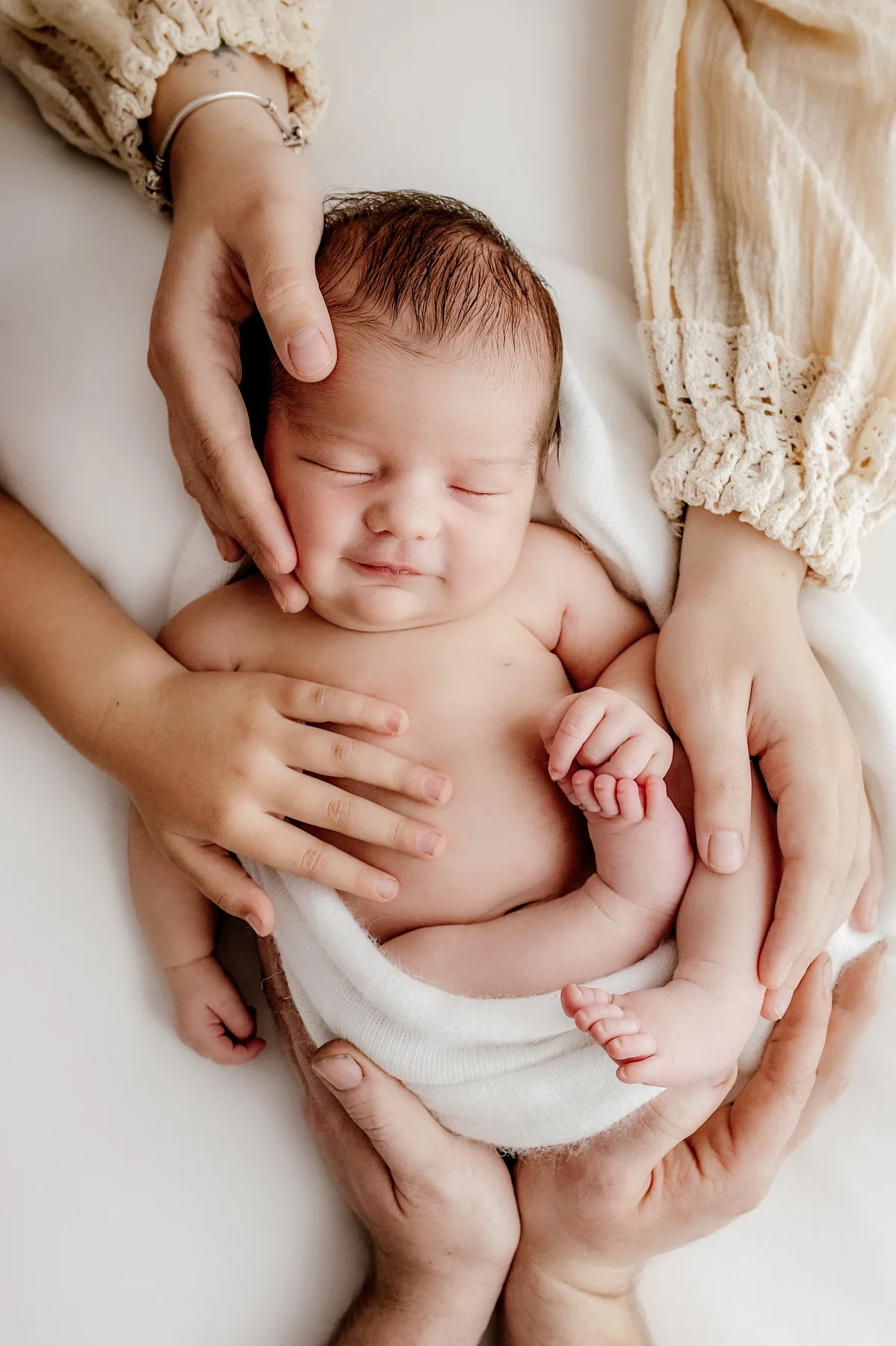Parent's hands gently holding a sleeping newborn