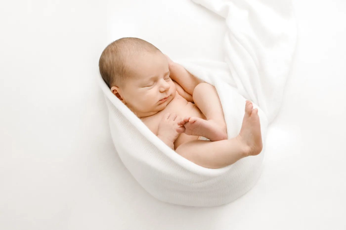 Newborn curled peacefully in a white wrap